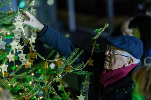 An elderly man reaching up for a gold star hanging on the Christmas tree
