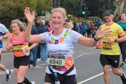 A woman in a Royal Marsden Running vest running along a London road and waving at supporters