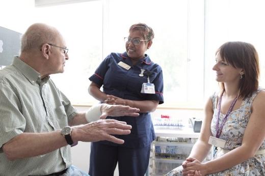 A patient sitting in a hospital room talking to two healthcare professionals who are smiling and listening to them intently