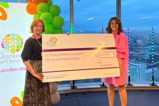 Two people holding a large cheque for £100,000 in front of Royal Marsden signage and balloons, at the top of London's BT Tower