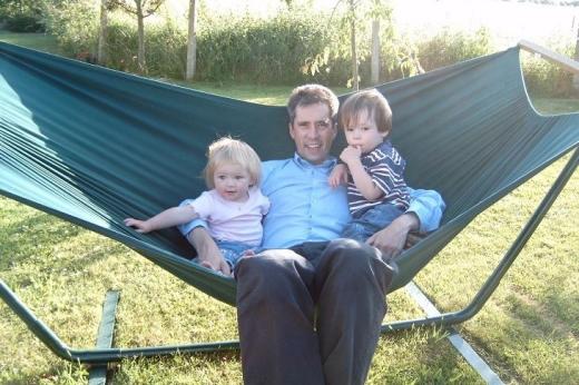 A father sitting on a hammock in the garden with his two small children