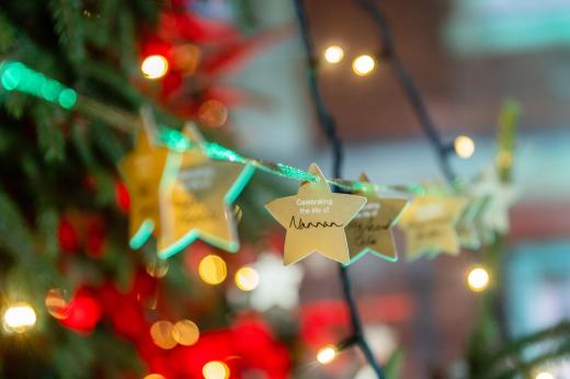 A close up of gold stars with names written on them, hanging on a Christmas tree with gold fairy lights