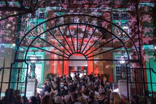 A group of people singing carols in front of The Royal Marsden hospital in Chelsea, which is lit up by colourful lights