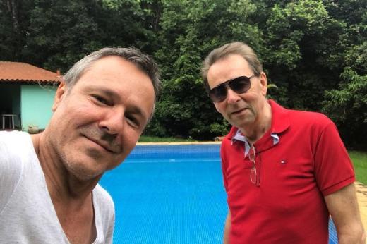 Two men taking a selfie in front of an outside swimming pool