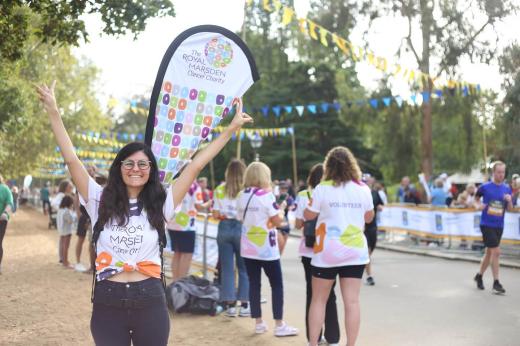 Woman in a Royal Marsden Cancer Charity t-shirt with her arms up, next to a road with people running and cheering