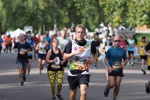A man running in a Royal Marsden Cancer Charity vest amongst other runners of the Royal Parks Half Marathon