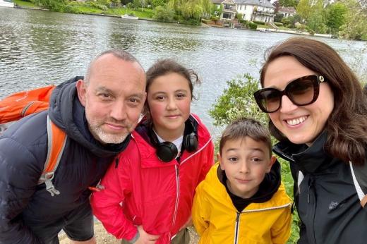 A family of four, including a mum, dad and two young children, standing and smiling on a river bank
