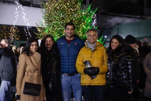 A family of five wrapped up warm in coats, standing in front of a large Christmas tree