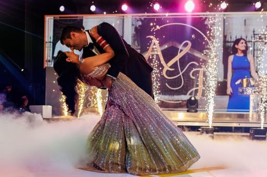 A man in a suit dancing with a woman in a beautiful sparkly dress on a stage with lights, fire effects and dry ice