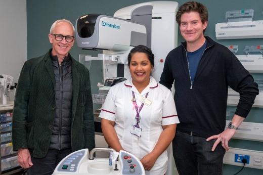 Three people, including a Royal Marsden Radiographer in uniform in the middle, standing in front of a large piece of white machinery in a hospital room