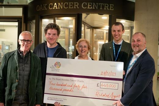 Five people standing outside of The Royal Marsden's Oak Cancer Centre, holding a large check for £445,000