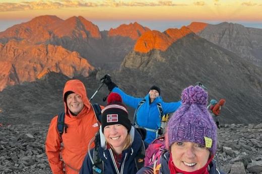 Four hikers smiling in front of a view of a beautiful mountain range at sunset