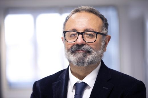 Headshot of a person in a suit and tie, with a beard and glasses