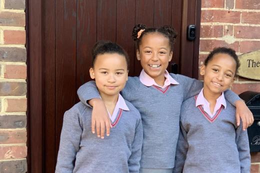 Three young school girls in grey uniforms standing and smiling in front of a door