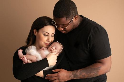 Two people looking down and smiling at a newborn baby 