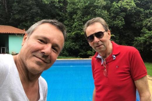 Two men taking a selfie in front of an outside swimming pool 