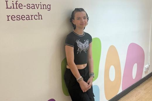 A young person smiling and leaning against a wall with Royal Marsden Cancer Charity branding
