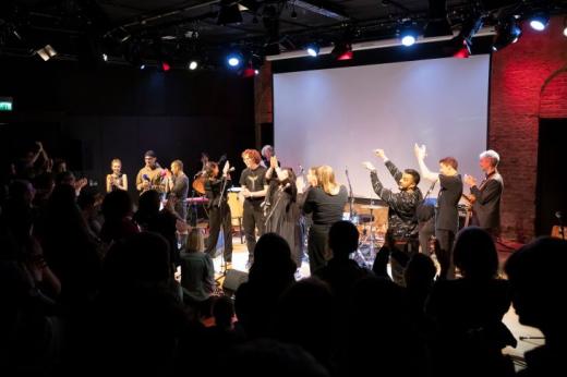 A group of young performers smiling and clapping on a stage in front of a crowd
