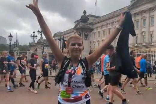 Team Marsden runner outside Buckingham Palace with her medal, smiling and waving her hands in the air