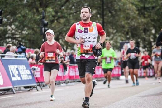 A person in A Royal Marsden Cancer Charity vest jogging along a road lined with a crowd 