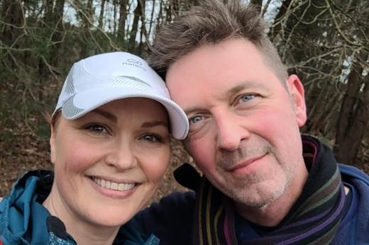 Two people smiling with their heads touching, on a walk in a wooded area