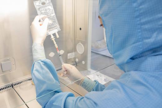 A Royal Marsden Nurse working in a sterile cellular therapies laboratory. She is wearing a blue sterile suit, gloves and mask and is using a syringe to pull liquid from a medication bag.