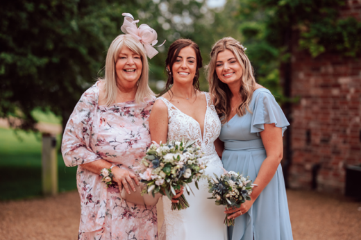 Nicola (left) with her daughters Jo and Sam standing outside in wedding outfits, smiling at the camera