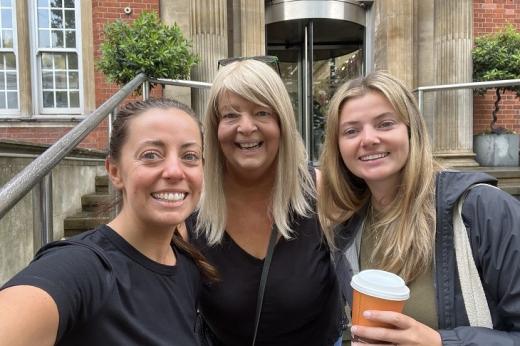 Royal Marsden patient Nicola in the middle of her two daughters, they are smiling and standing on the main entrance steps of The Royal Marsden in Chelsea