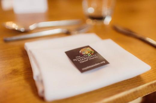 A Royal Marsden Cancer Charity wedding pin sitting on a serviette at a wedding table