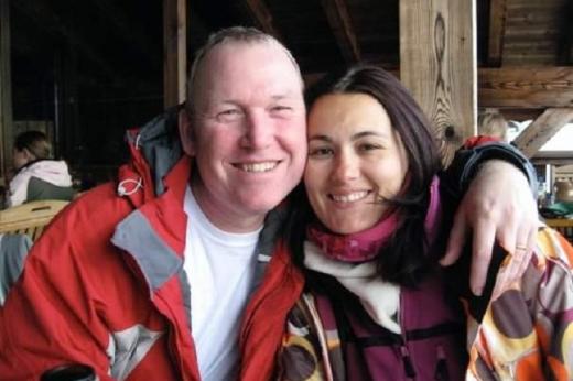 A married couple sitting in warm clothing, with their arms around each other