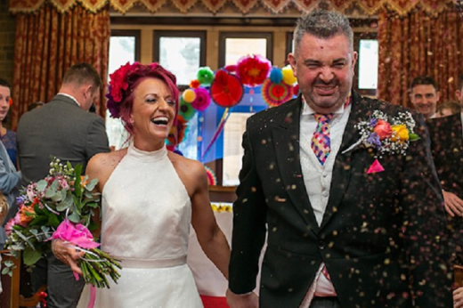 A smiling and happy husband and wife walking down the aisle while wedding guests throw confetti on them.