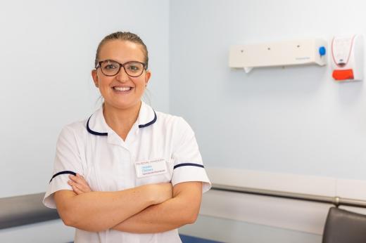 A physiotherapist in a white uniform, smiling and crossing her arms in a medical room in The Royal Marsden
