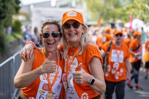 Two women wearing orange, smiling and doing a thumbs up sign