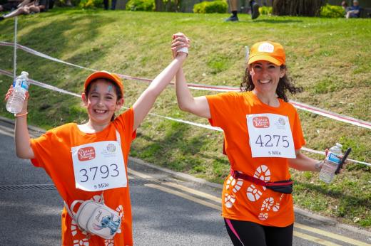 A woman and girl holding hands smiling, wearing orange tops
