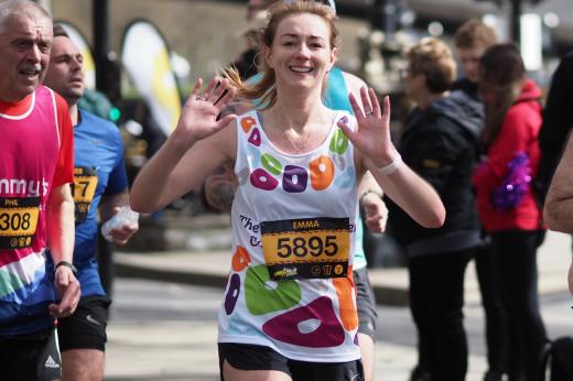 Runner in RMCC vest waves at camera as she passes