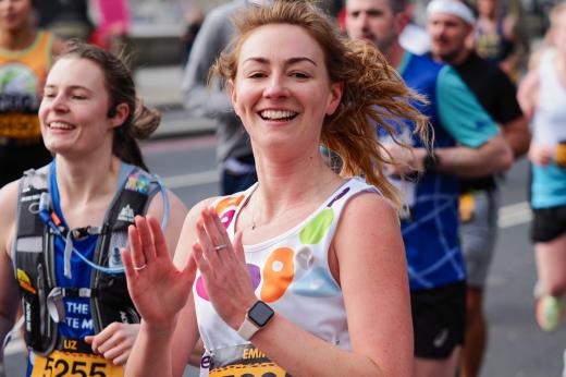 Runner smiles and claps in Royal Marsden Cancer Charity vest 