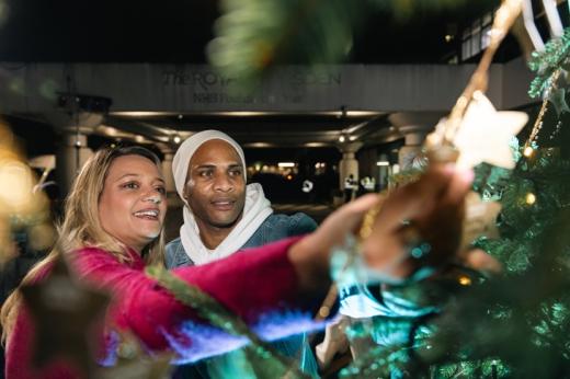 A woman and man reaching up to a star on a Christmas tree