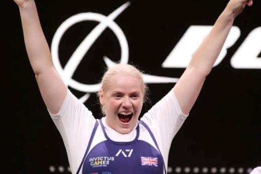 Amanda in an Invictus games leotard, she's at an event, smiling wide and has her arms up.