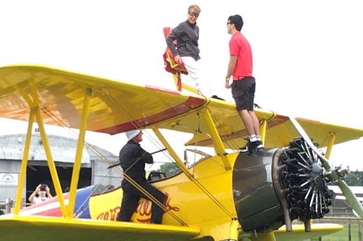 Marilyn being strapped into safety harnesses on top of a yellow, double winged propeller plane.