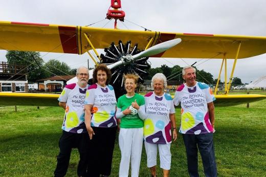 A group of five people wearing Royal Marsden Cancer Charity t-shirts and standing in front of a yellow propeller plane