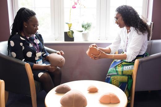 Two members of staff from The Royal Marsden sitting at at table. They are holding and looking at a selection of soft breast-shaped prosthetics, which are in a variety of sizes and skin tones