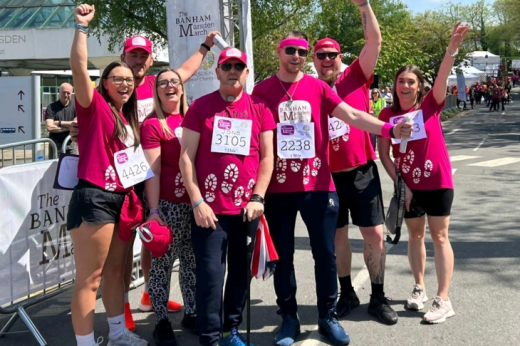 Jon standing in the middle of his Banham Marsden March team, at the Sutton hospital finish line. They are all cheering and wearing bright pink t-shirts and hats