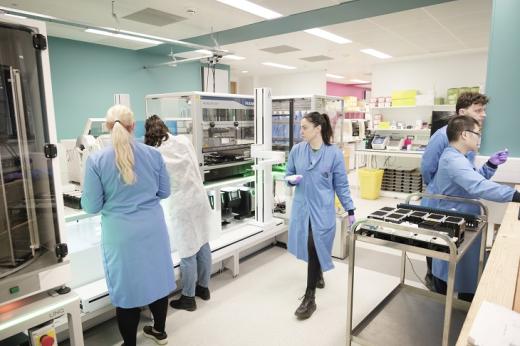 A laboratory team in blue lab coats, looking at a large robotic machine