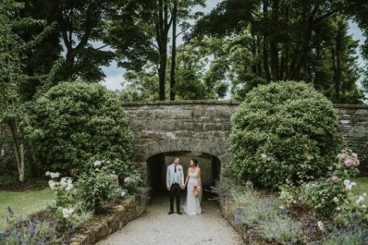 A bride and groom holding hands outside next to a bridge