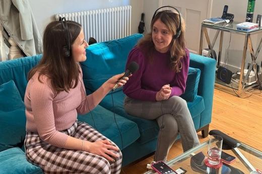 Shiona and an interviewer from the BBC. They are both wearing headphones and sitting on a sofa in a living room. The interviewer is speaking to Shiona while holding up a microphone.