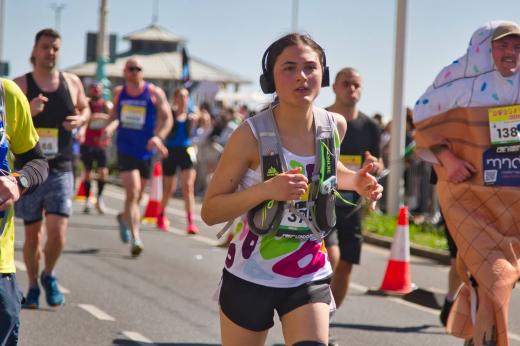 Royal Marsden runner running with headphones on and a running vest. There is a runner on the right of her dressed in an icecream costume.