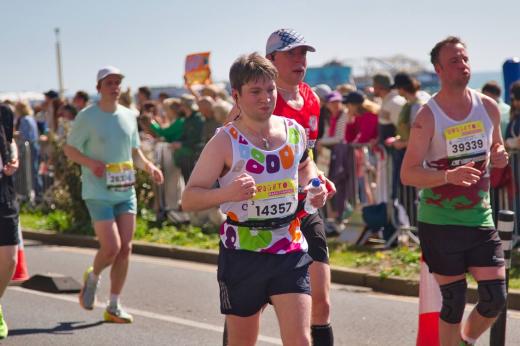 Royal Marsden runner running with others, looking worn out. Runner has headphones in and has the pier faintly in the background of the photo.