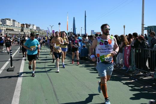 Royal Marsden runner with other runners next to him, all running past cheering supporters along the seafront.