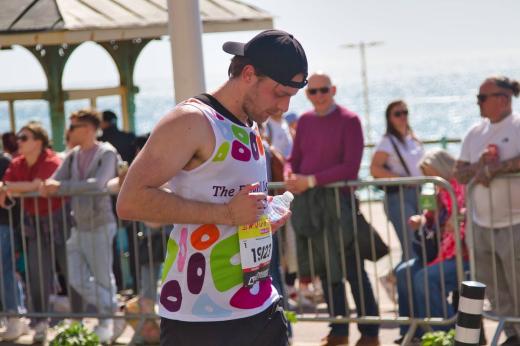 Royal Marsden runner with hat backwards and facing down concentrating. There are supporters in the background standing behind a fence. 