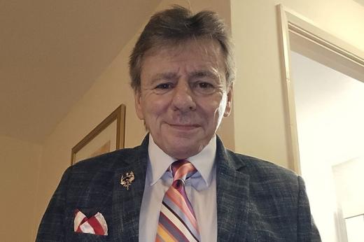 Royal Marsden patient, Steve. He has short, grey hair and is wearing a dark grey suit jacket, with a pale shirt, brooch and colourful-striped tie.